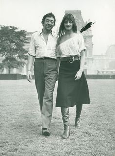 an old black and white photo of a man and woman walking in the grass together