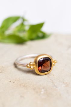 This handcrafted ring features a deep red garnet, elegantly set in a rich gold bezel, beautifully contrasting with the slender silver band. The delicate gold accents on either side of the garnet add a playful touch, creating a more casual feel. This piece can easily be combined with a casual oufit or really be accentuated by combining it with a red or black cocktail dress. Sterling silver  Gold vermeil  Garnet  To properly care for your silver jewellery, there are a few important steps you shoul Rings Mixed Metals, Mixed Metals Jewelry, Garnet Ring Gold, Gold Garnet Ring, Cushion Cut Ring, Mixed Metal Jewelry, August Birthstone Jewelry, July Birthstone Jewelry, Garnet Ring