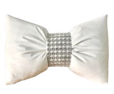 a white bow pillow with silver sequins on the front and back, sitting against a white background