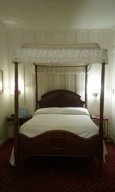 a four poster bed in a room with red carpeting and white sheets on it