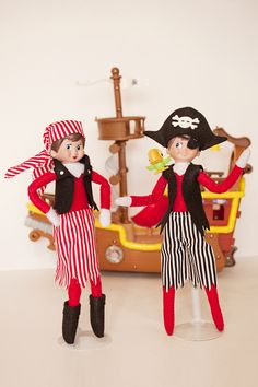 two dolls dressed in pirate costumes standing next to each other on a white surface with a ship in the background