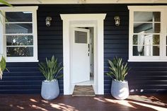 two large planters on the front porch of a blue house with white doors and windows