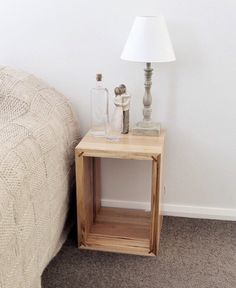 a small wooden table next to a bed with a lamp on it and a white wall in the background