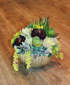 an arrangement of succulents and flowers in a basket on a wooden floor