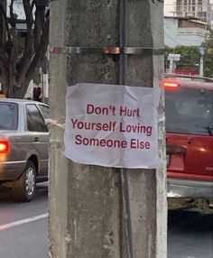 a sign attached to a pole on the side of a road that says don't hurt yourself loving someone else