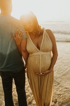 a pregnant woman standing next to a man on the beach