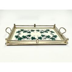 a metal tray with green leaves on it and handles, sitting on a white surface