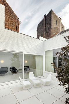 two white chairs sitting on top of a tiled floor next to a tree and building