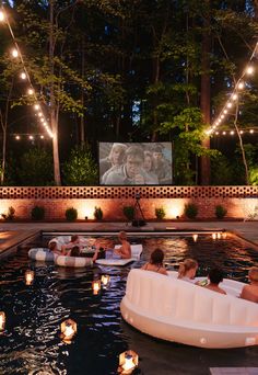 an outdoor movie is being projected on the wall next to a pool with people in it