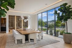 a dining room table with white chairs next to a large glass window and potted plant