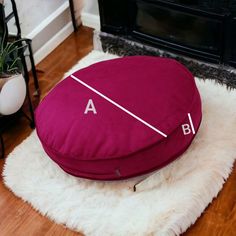 a red round pillow sitting on top of a white rug next to a fire place