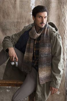 a man sitting on top of a wooden bench wearing a jacket and scarf over his head