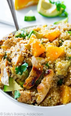 a white bowl filled with chicken and rice next to sliced oranges, cucumbers and cilantro