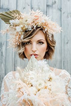 a woman with flowers in her hair holding a fan and looking at the camera while standing next to a wooden wall