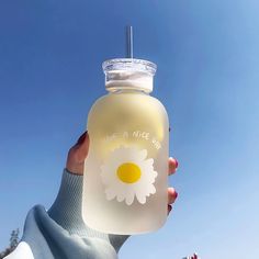 a person holding up a plastic bottle with a flower on the front and one side