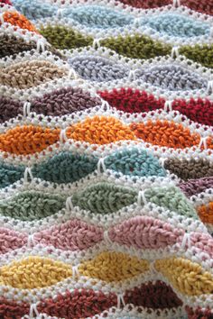 a crocheted blanket is laying on top of a tablecloth that has multicolored stripes