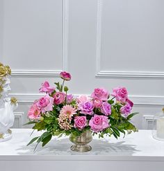 a vase filled with pink and purple flowers on top of a table next to two statues