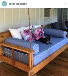 a dog laying on top of a wooden swing bed with blue sheets and white pillows