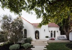 a white house with steps leading up to the front door and entry way, surrounded by greenery