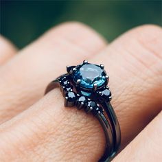 a woman's hand holding a ring with an aqua stone in the center and black diamonds around it