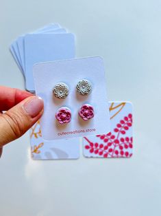 a person is holding two pairs of pink flower studs in front of a card