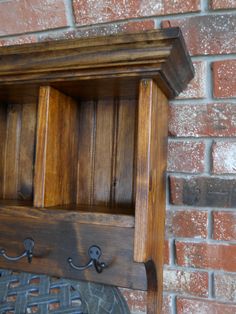 a wooden shelf with hooks on it against a brick wall