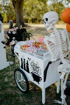 a skeleton sitting on top of a white cart filled with candy next to a tree