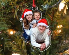 a christmas ornament hanging from a tree with a family wearing santa hats on it