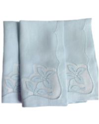 two white napkins with embroidered flowers on the front and one is folded in half