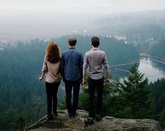 three people standing on top of a mountain looking out at the valley and lake below