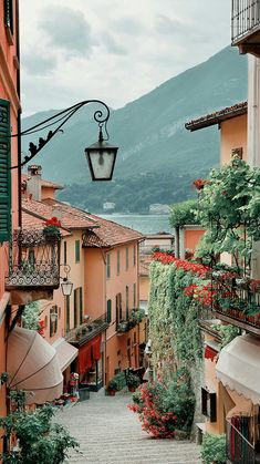 an alley way with flowers and umbrellas on the side, in front of mountains