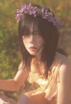 a young woman with flowers in her hair sitting on the ground next to some grass