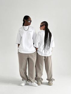 two people standing next to each other wearing white shirts and khaki sweatpants