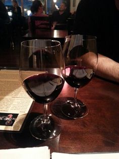 two glasses of red wine sitting on top of a table next to an open book