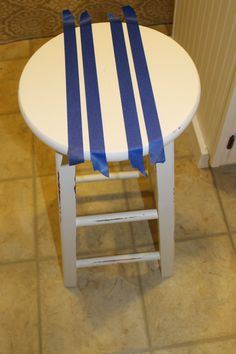 a small white table with blue stripes on it and a wooden stool in the corner