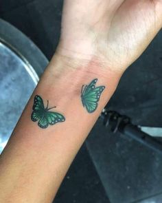 a small green butterfly tattoo on the wrist