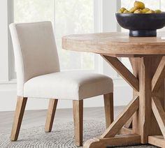 a bowl of fruit sitting on top of a wooden table next to a white chair