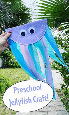 a paper plate jellyfish craft is being held up by a woman's hand