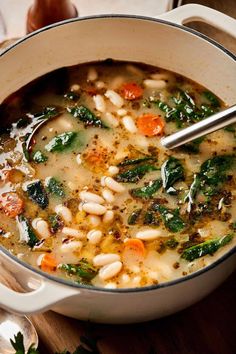 a pot filled with soup and vegetables on top of a wooden table next to utensils