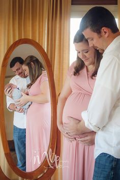 a man and woman standing in front of a mirror holding their baby bumping it's belly