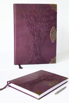 a purple book with a tree design on the front and side, next to a pen