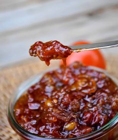 a spoon full of jam with tomatoes in the background