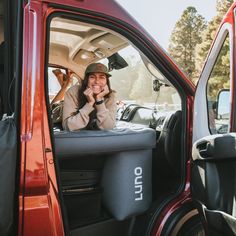 a woman sitting in the drivers seat of a red truck with her hand on her chin