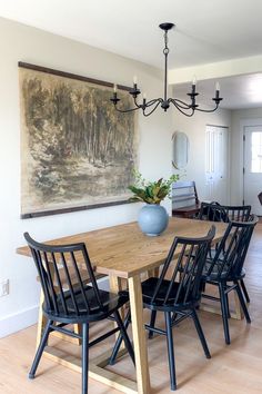 a dining room table with black chairs and a painting on the wall