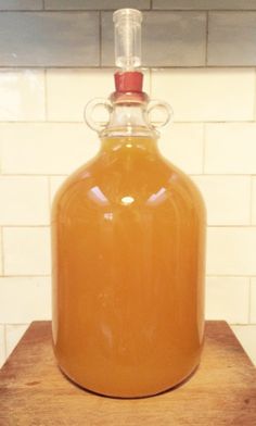 a glass bottle filled with liquid sitting on top of a wooden table next to a white tiled wall