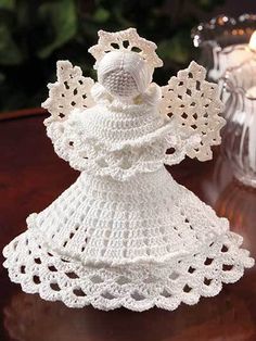 a crocheted angel figurine sitting on a table next to a lit candle