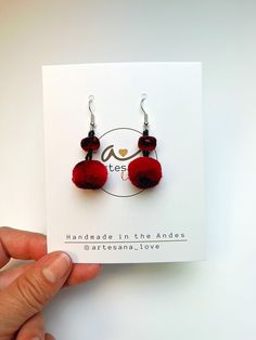 a pair of red pom - poms hanging from earrings on a white card