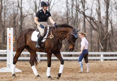 a woman riding on the back of a brown horse next to a girl in blue jeans