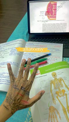 a person's hand with tattoos on it next to an open book and laptop