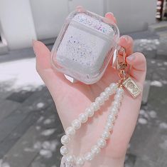 a hand holding an apple airpods case with pearls and a keychain attached to it